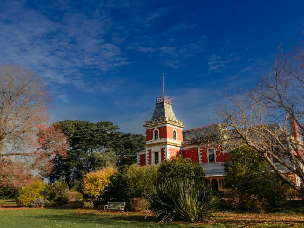 Coolart homestead surrounded by autumn trees with a blue sky and dusty white clouds.