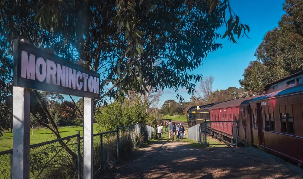 Tourist steamtrain stopped at the old Mornington Station with people walking up the ramp to the train.