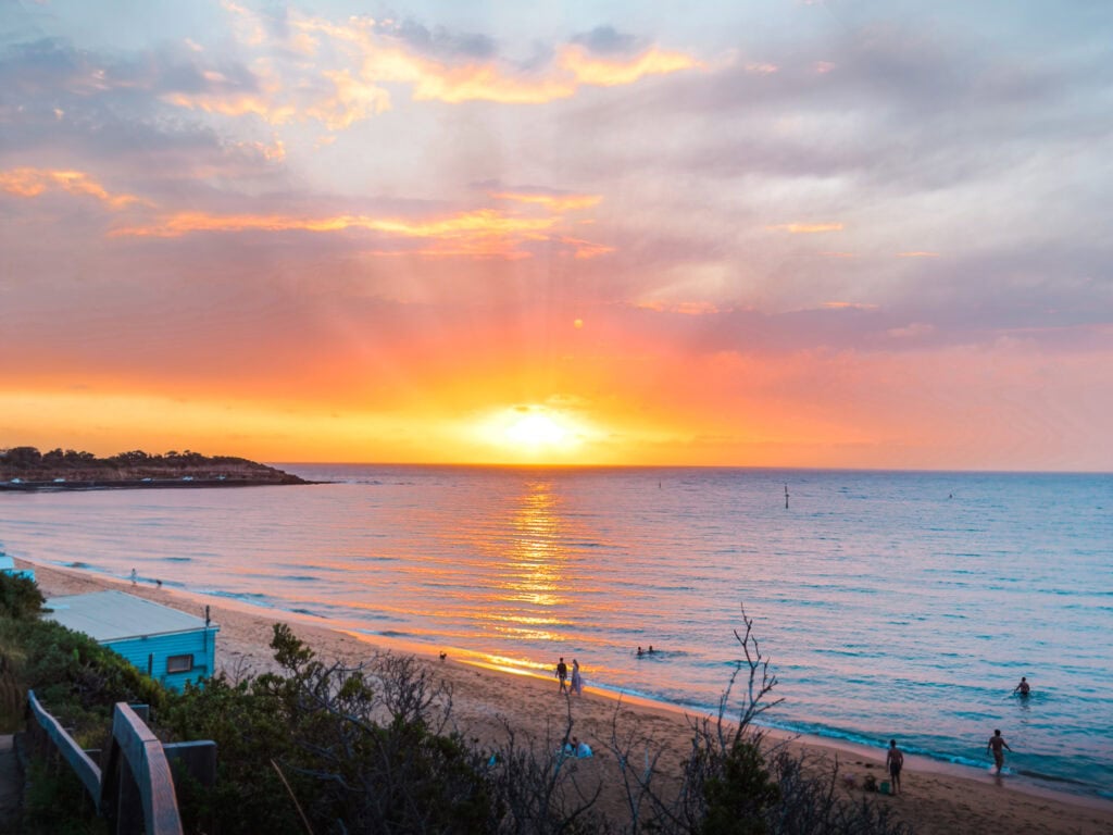 View from the top of a cliff looking over the water of Fishermans Beach with the sun setting in the background on a summer's evening.