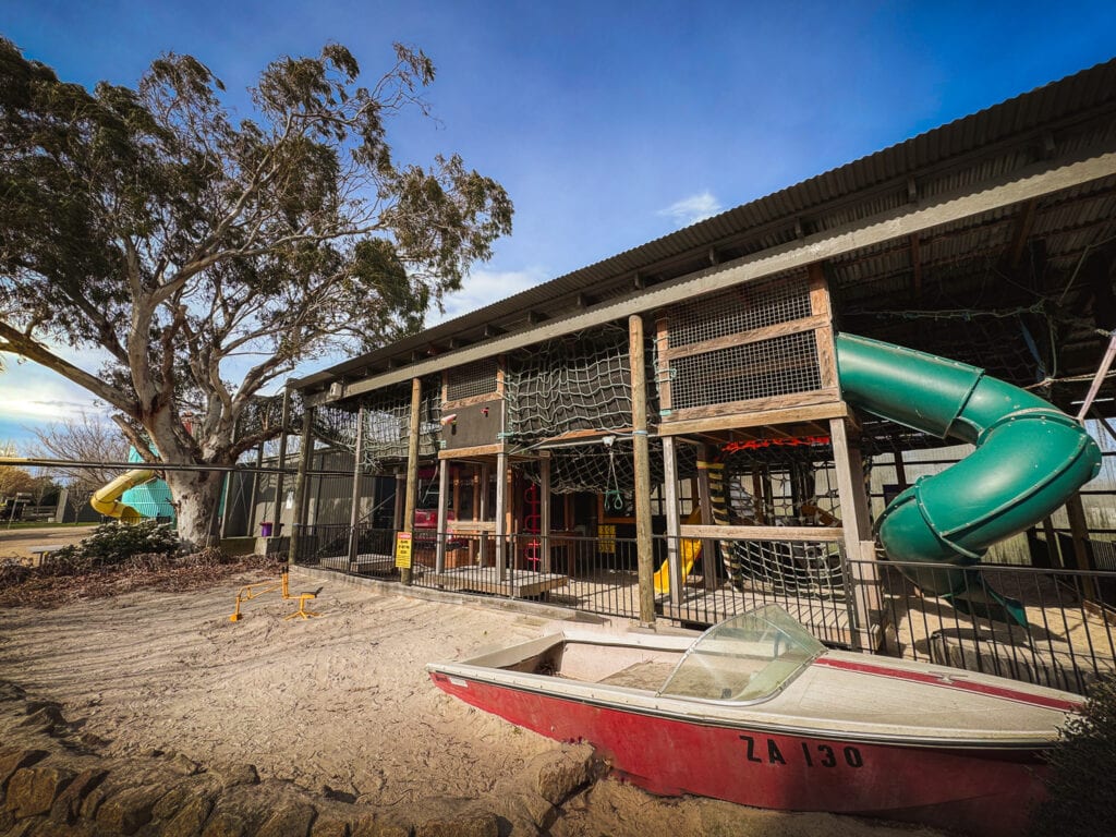 A view from a distance of the outside of the adventure playground. You can see the play boat and long green twirly slide.