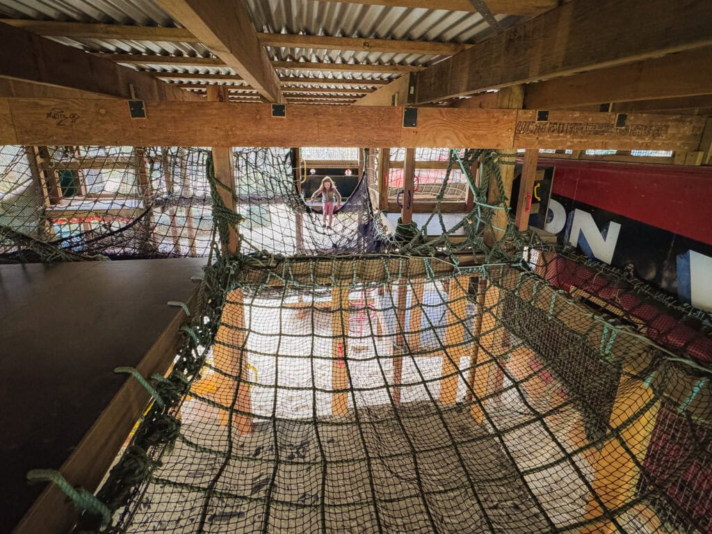 A view across the big netted area inside the adventure playground. There's a young girl in the centre climbing.